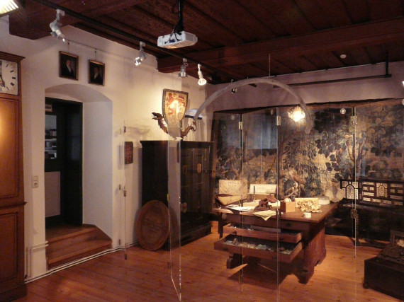 Blick in die Wunderkammer der Sonderausstellung. Im Vordergrund ein Tisch mit Schreibutensilien, im Hintergrund eine prächtige Tapisserie.